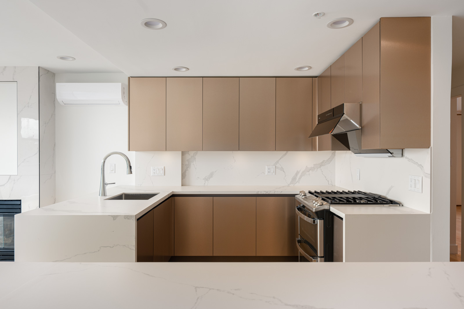 Modern kitchen with brown cabinets, white marble countertops and backsplash, stainless steel appliances, and a built-in stove with a range hood.