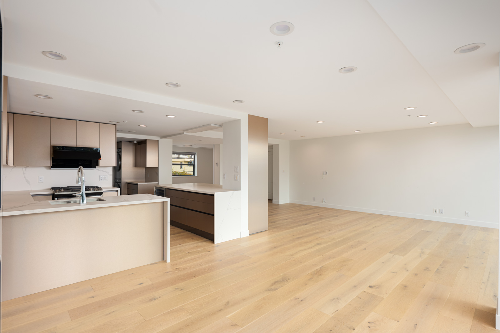 Spacious modern kitchen and living area with light wood floors, recessed lighting, and neutral-colored cabinets in an open floor plan.