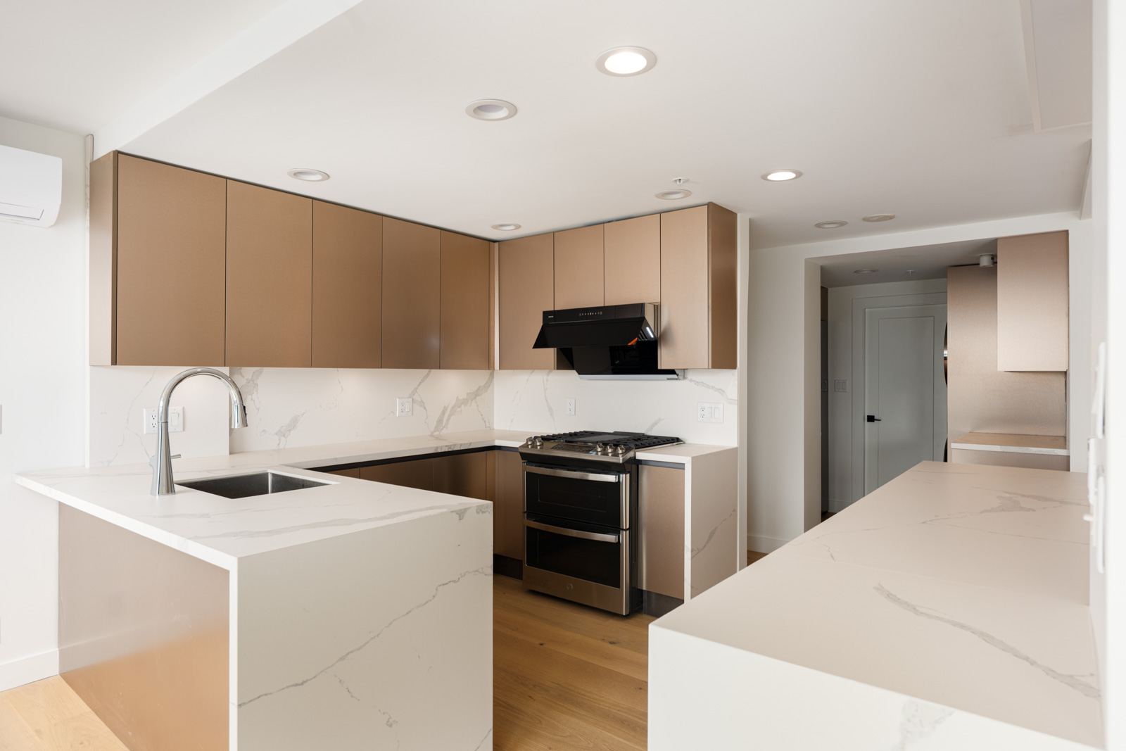 Modern kitchen with beige cabinets, a black stove and hood, built-in sink, marble countertops, and wood flooring under recessed lighting.
