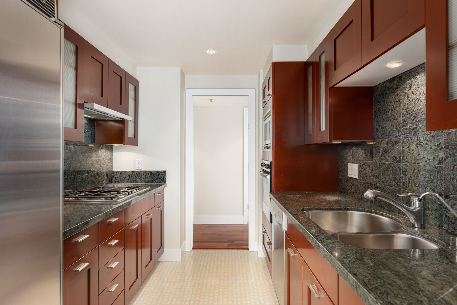Modern galley kitchen with dark wood cabinets, stainless steel appliances, double sink, and green marble countertops.