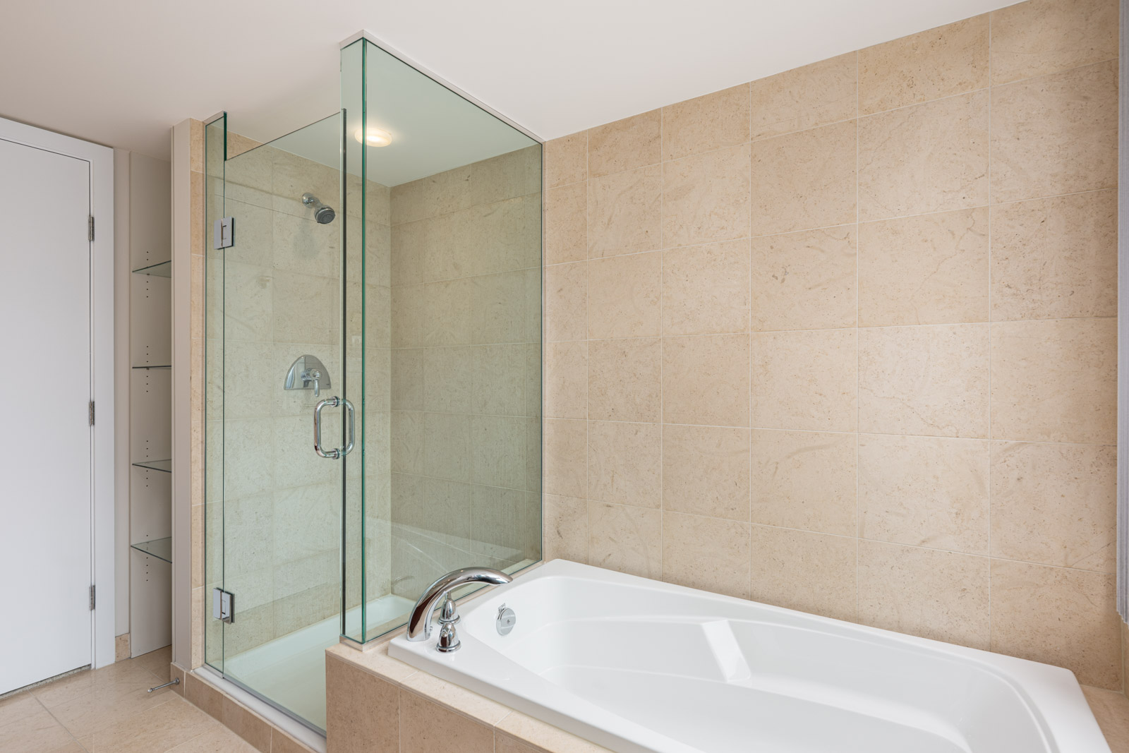 Modern bathroom with a glass-enclosed shower and a separate bathtub, both surrounded by beige tiled walls and flooring.