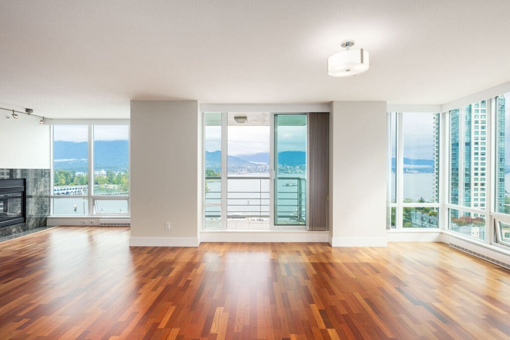 Unfurnished modern apartment with wood flooring, large windows, and a balcony overlooking water and mountains.