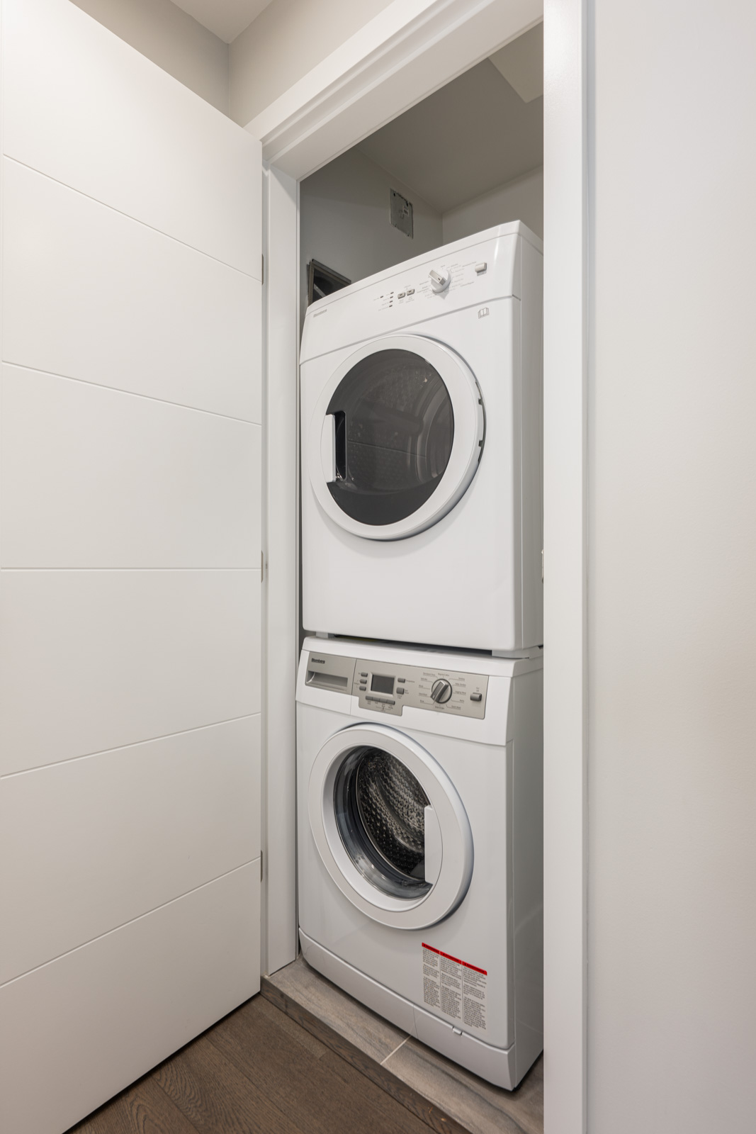 A stacked washer and dryer set is placed inside a small, white closet with the door partially open, showing a compact laundry area.