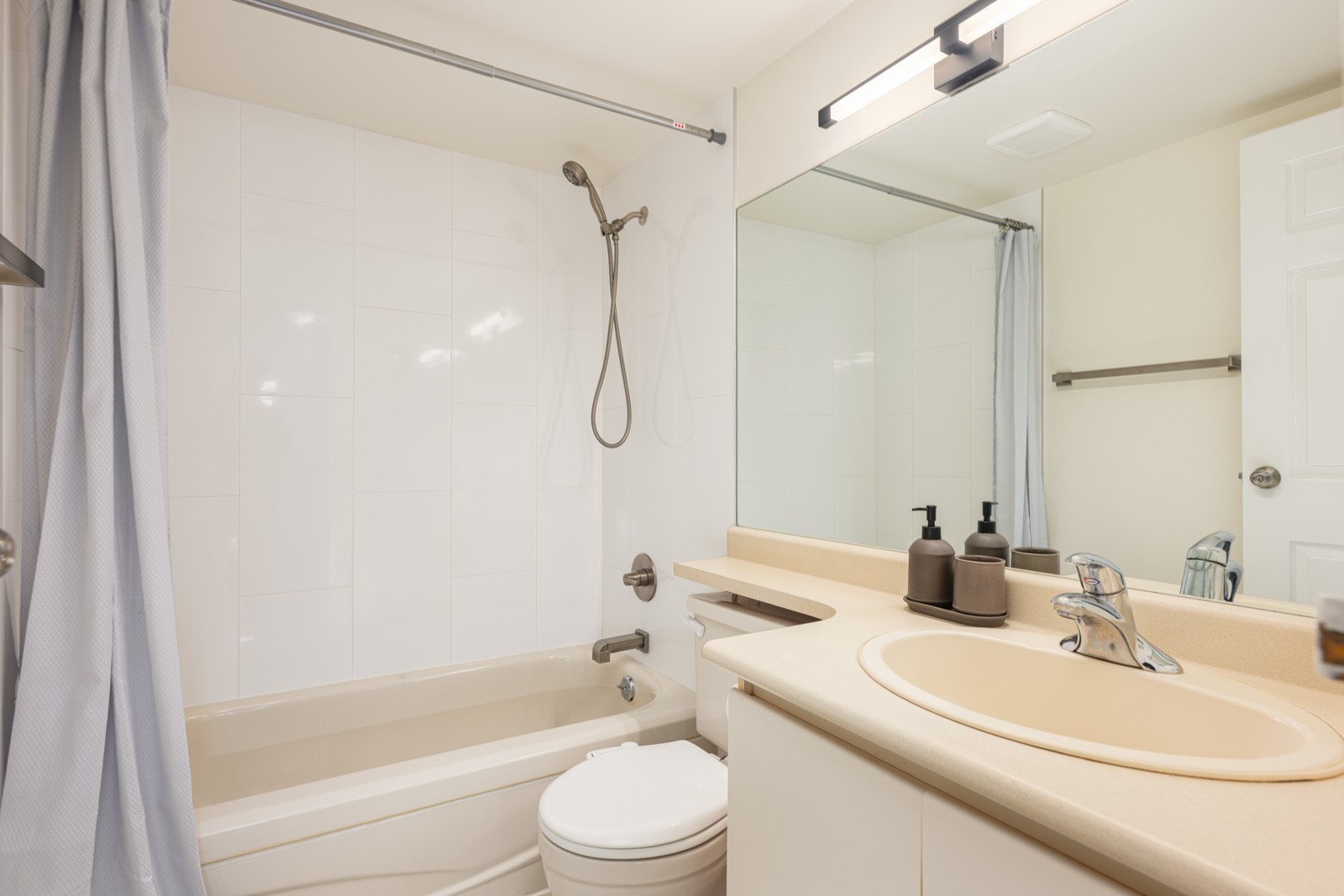Modern bathroom with a bathtub, wall-mounted showerhead, toilet, light-colored countertop with sink, and a large mirror above the vanity.