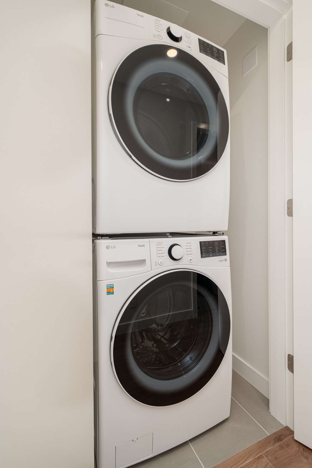 A stacked front-loading washer and dryer set in a small, white-walled laundry closet with a tiled floor.