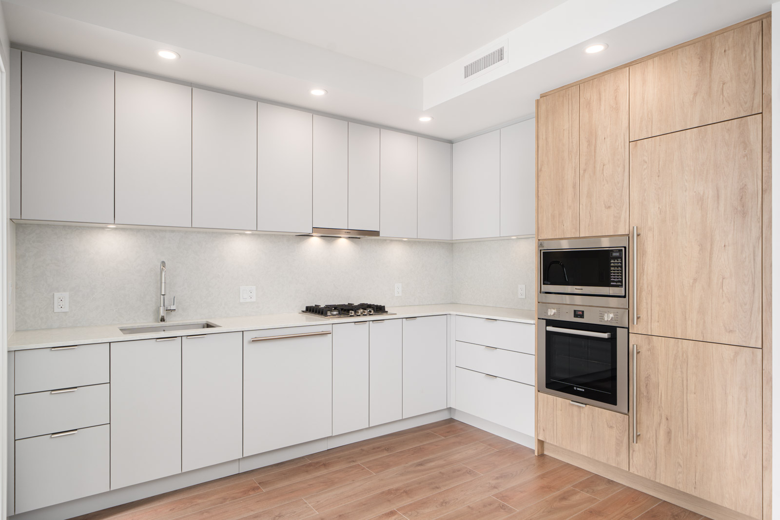 Modern kitchen with white cabinets, integrated appliances, wood accents, under-cabinet lighting, and light wood flooring.