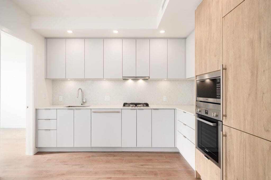 Modern kitchen with white cabinets, built-in oven and microwave, gas cooktop, sink, light wood flooring, and minimalist design.