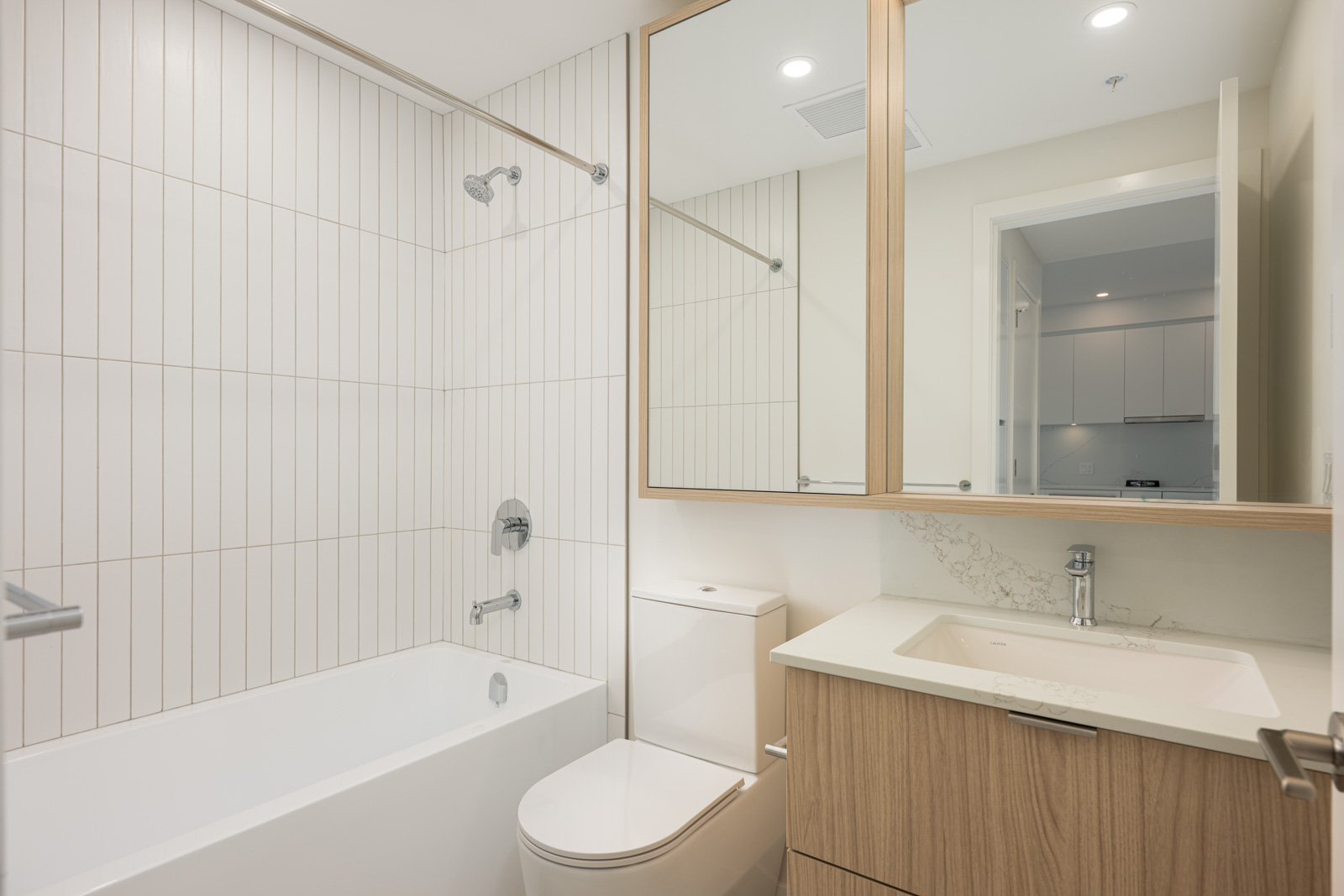 Modern bathroom with a bathtub-shower combo, vertical white tile, wall-mounted mirror cabinets, toilet, and sink with wood cabinetry.