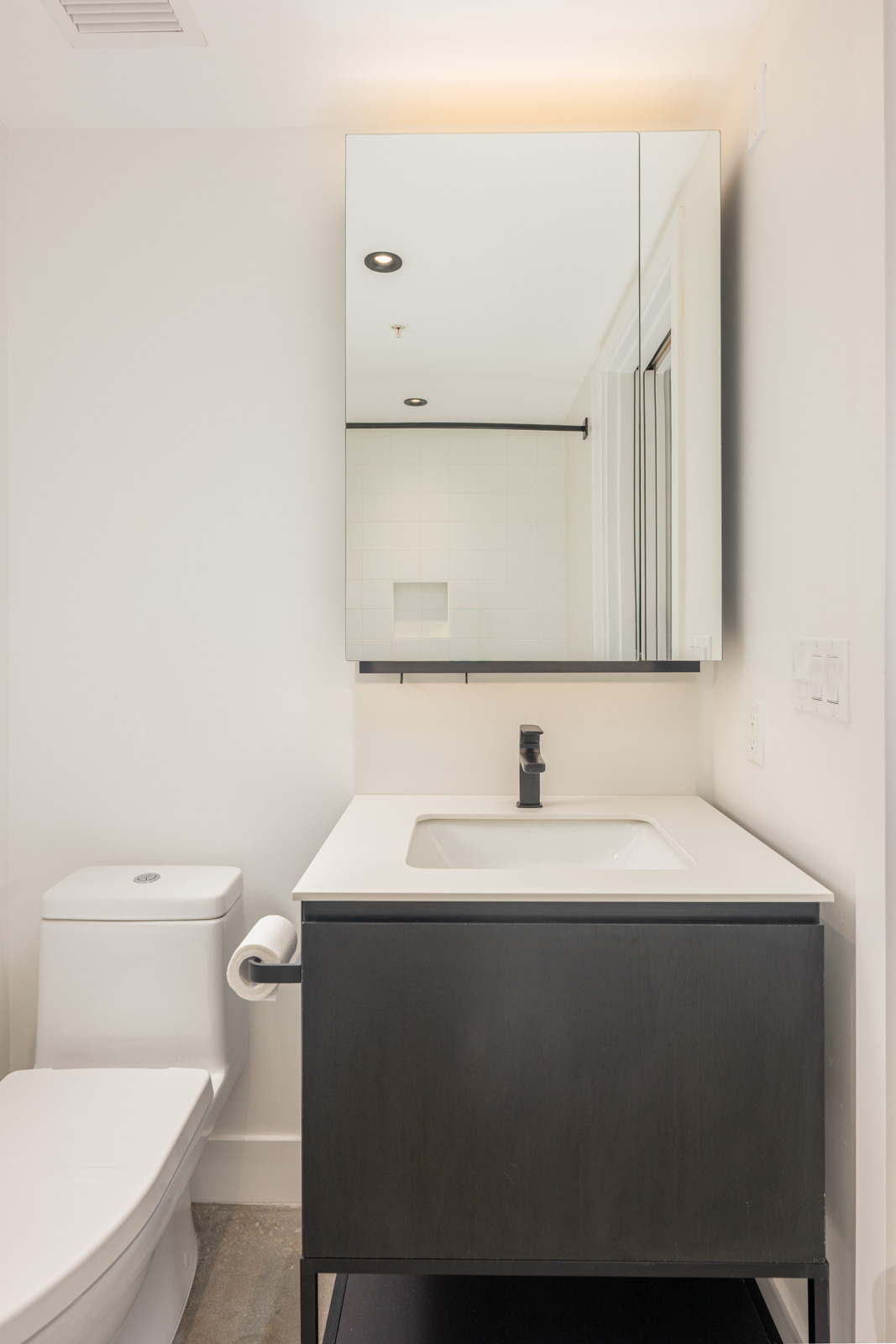 Modern bathroom with a white toilet, black vanity with sink, wall-mounted mirror cabinet, and white walls.