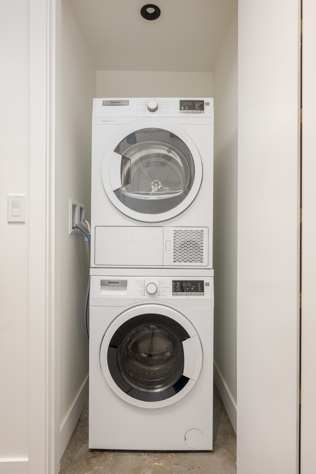 A stacked washer and dryer set inside a small laundry closet with white walls and a concrete floor.
