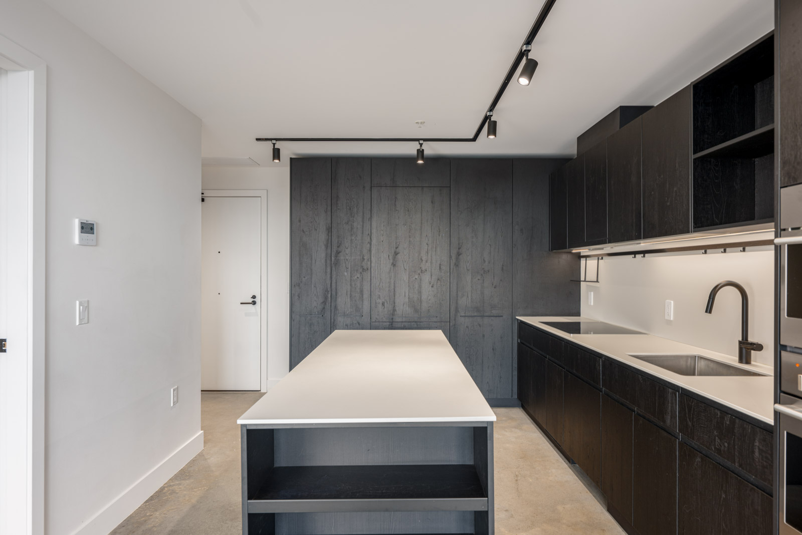 Modern kitchen with dark wood cabinets, a central island with open shelving, white countertops, and track lighting on a white ceiling.