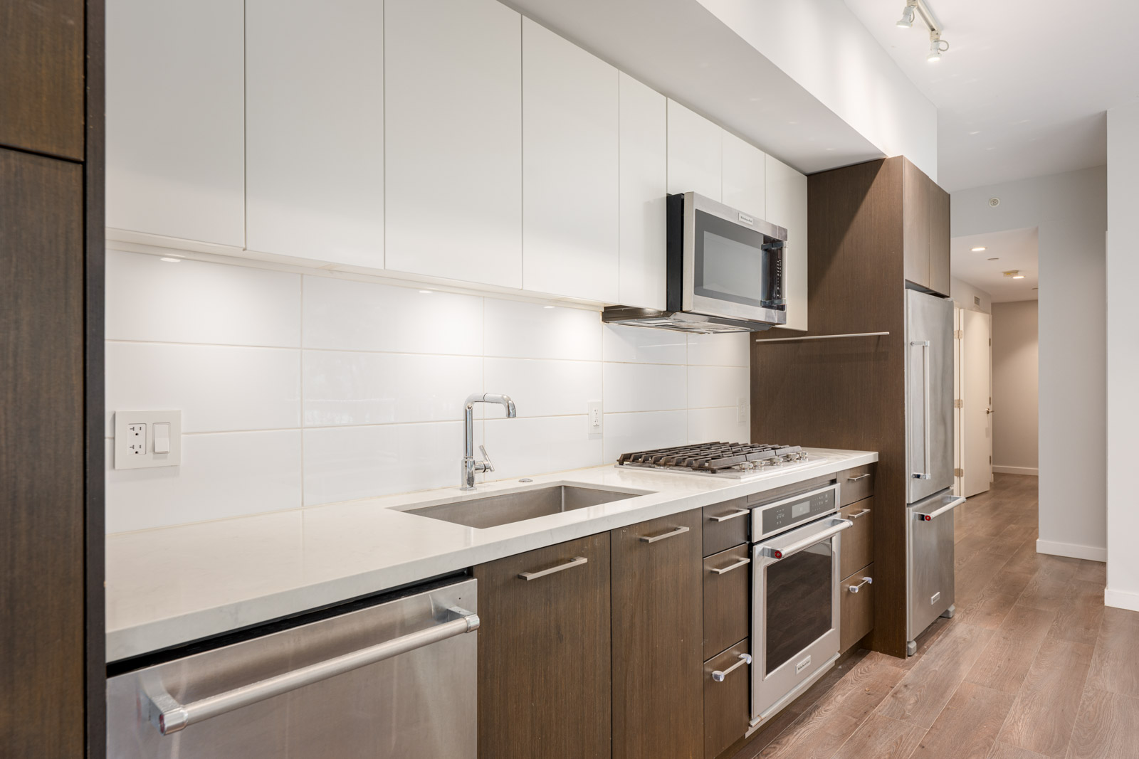Modern kitchen with white upper cabinets, dark lower cabinets, stainless steel appliances, gas stove, built-in oven, and light wood flooring.