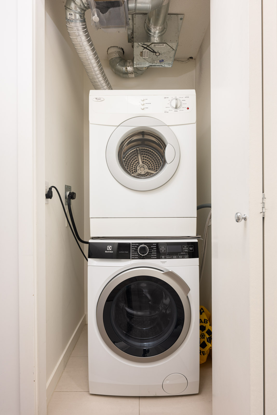 Stacked washer and dryer units in a small laundry closet with visible ventilation ducts above.
