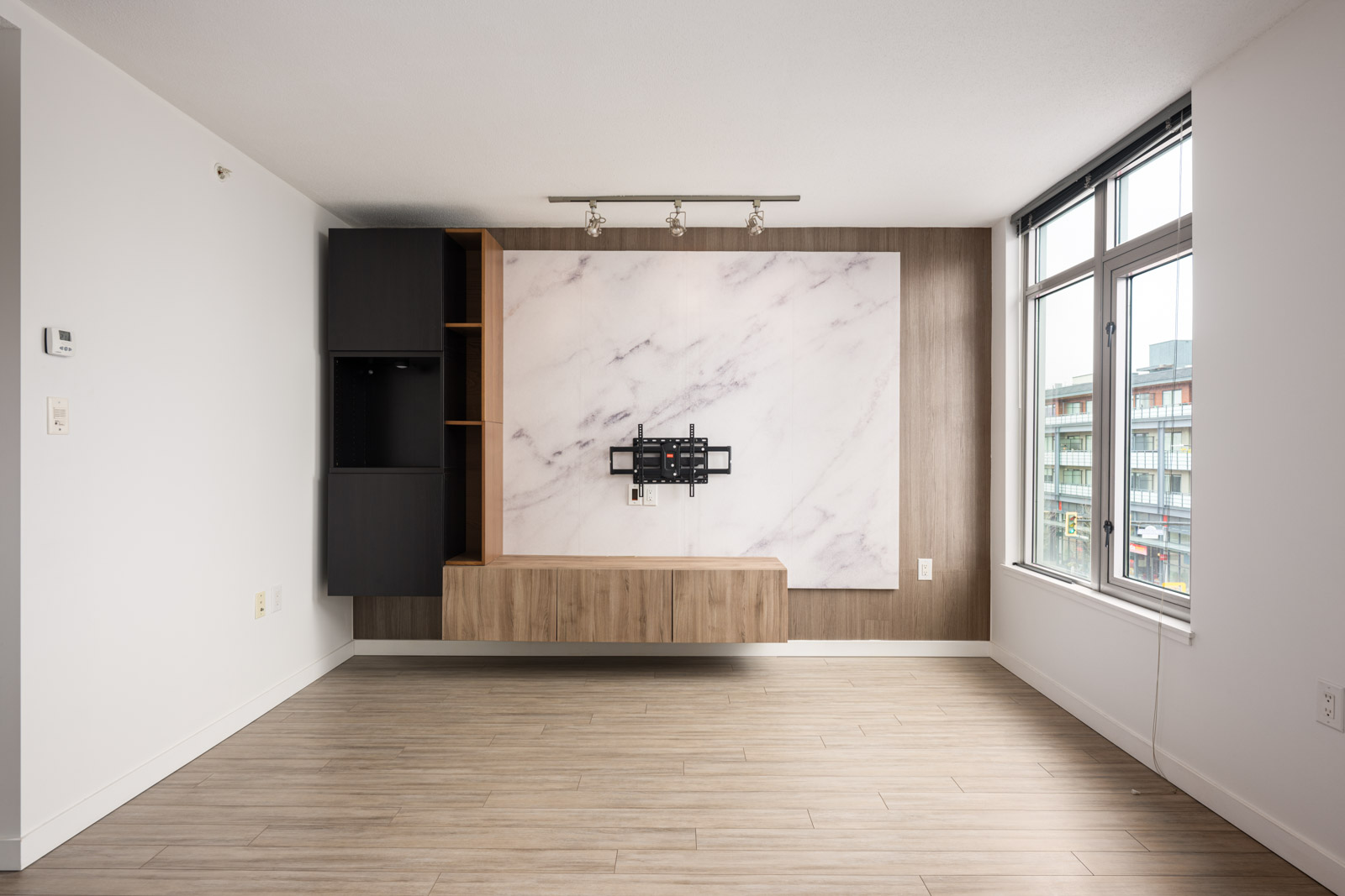 Minimalist living room with a wall-mounted TV stand, marble panel accent, wooden flooring, large window, and built-in shelving.