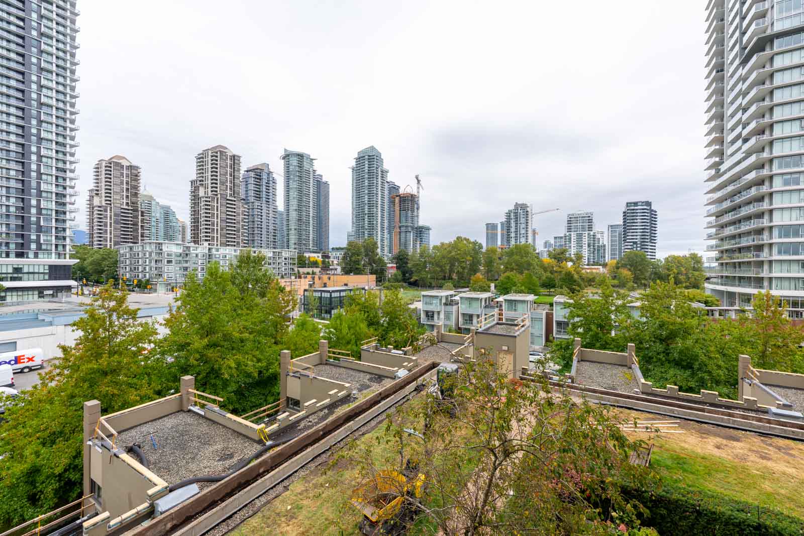 High-rise apartment buildings surround a green area with railway tracks and construction equipment in the foreground on an overcast day.