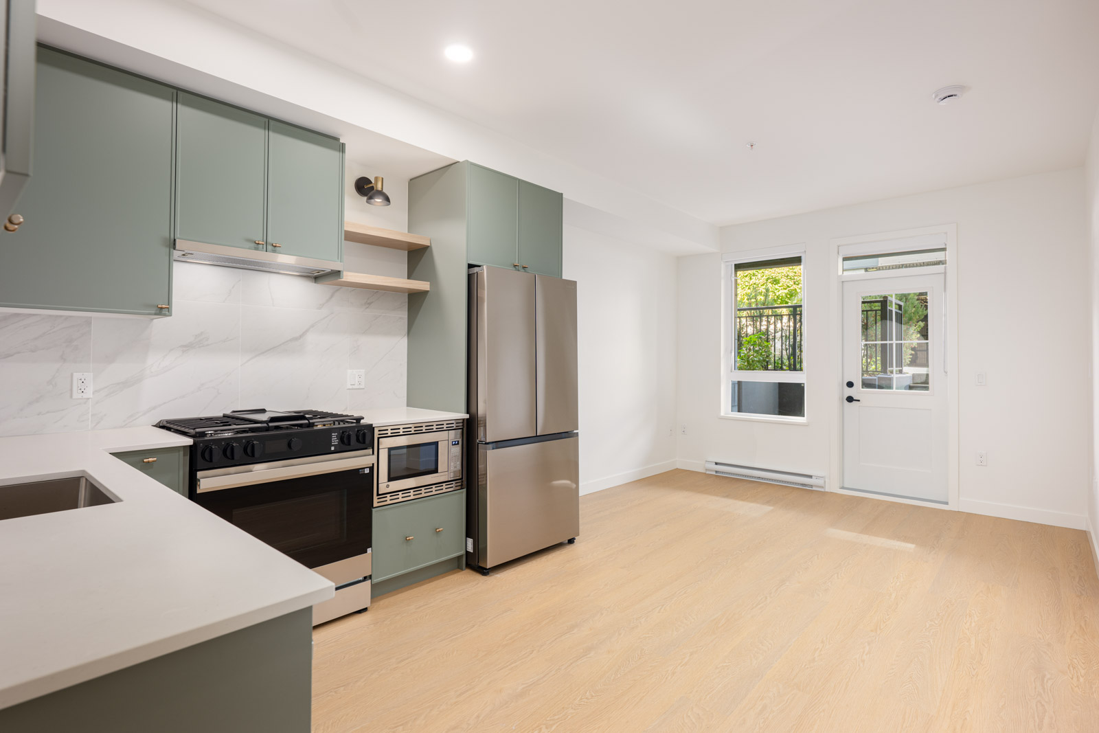 Modern kitchen with green cabinets, stainless steel appliances, light wood flooring, and a door leading to an outdoor area.