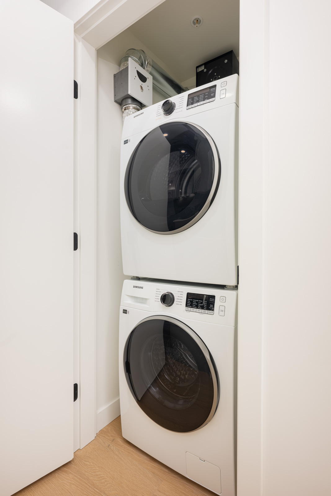 A stacked washer and dryer set installed in a small white laundry closet with the closet door partially open.