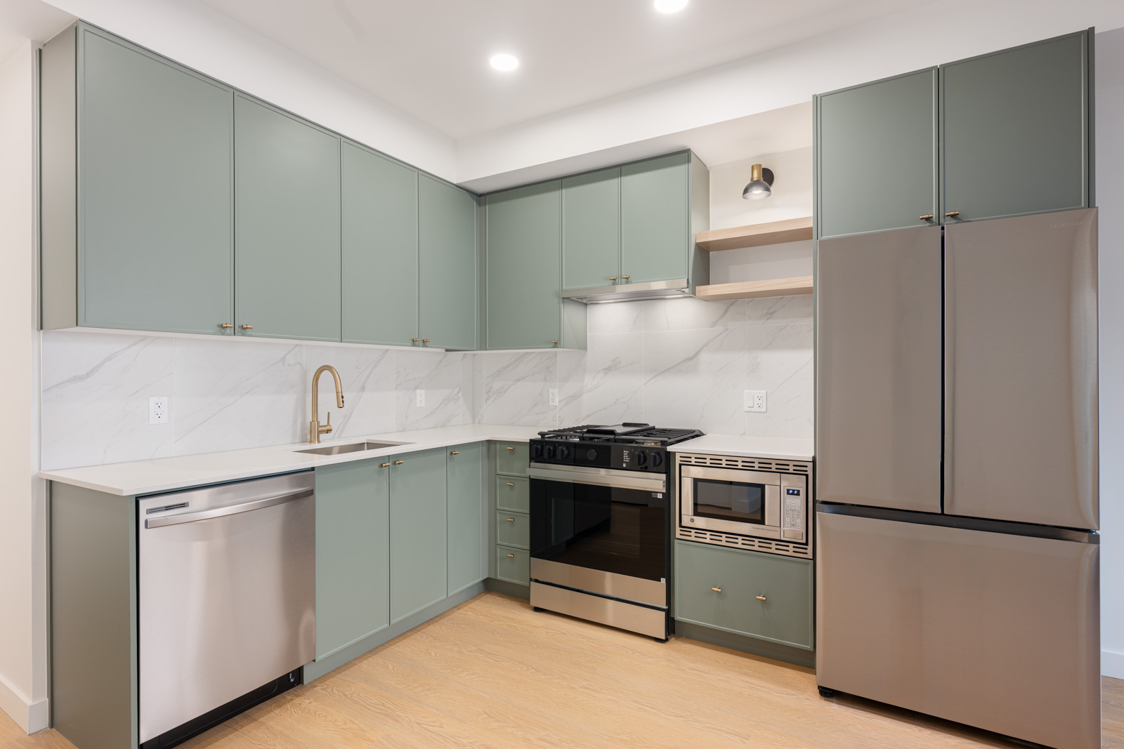 Modern kitchen with green cabinets, stainless steel appliances including a refrigerator, oven, microwave, dishwasher, and a marble backsplash.