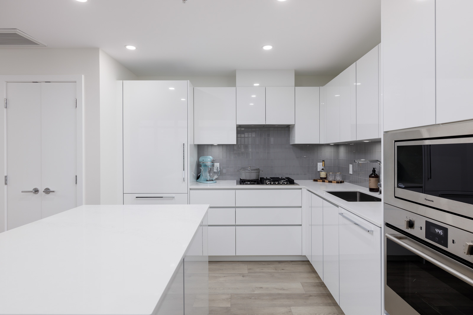 Modern kitchen with white cabinets, a central island, built-in appliances, a gas stove, and light wood flooring. Mixer and utensils are visible on the countertop.