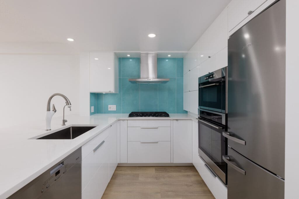 Modern kitchen with white cabinets, stainless steel appliances, a sink with a tall faucet, and a turquoise backsplash behind the stove and range hood.