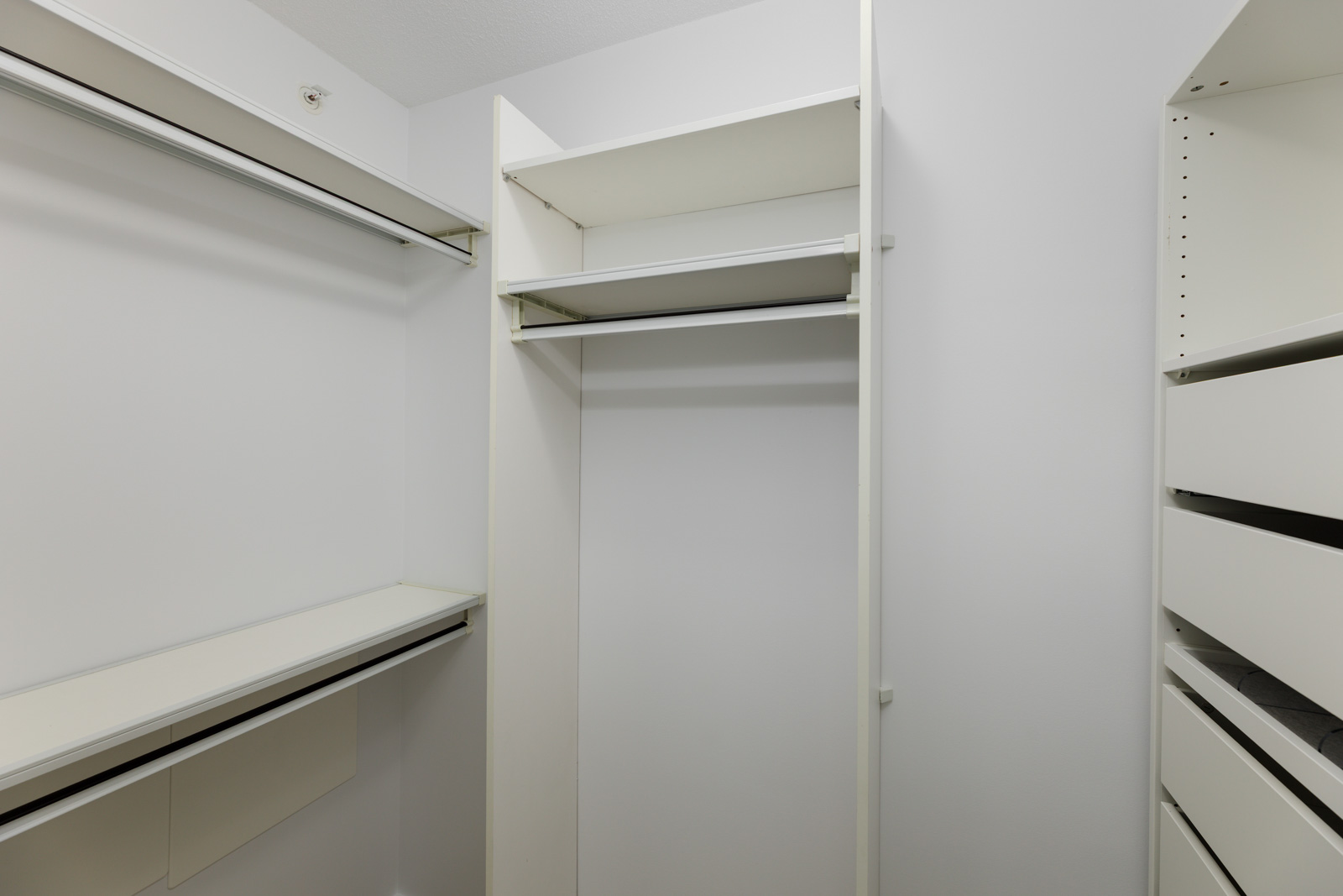 Empty white walk-in closet with built-in shelves, drawers, and hanging rods, featuring clean lines and a minimalist design.