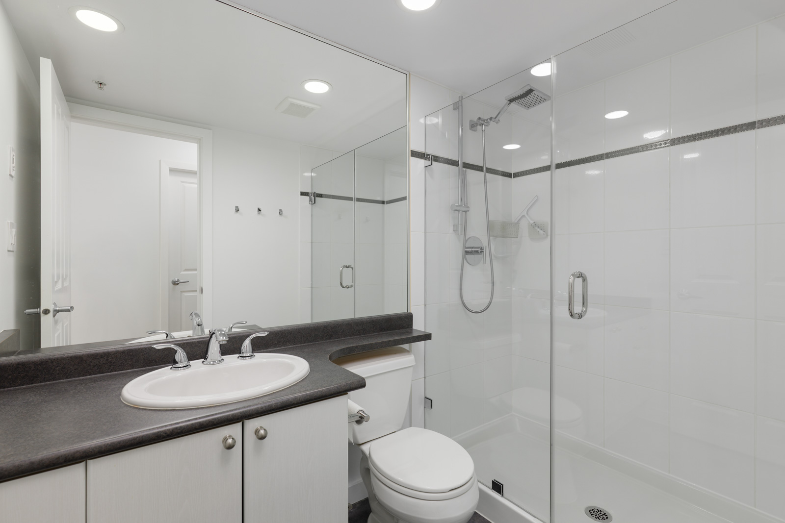 Modern bathroom with a white sink, countertop, toilet, and a glass-enclosed shower with a rainfall showerhead. White tiles line the shower and walls. Three hooks are mounted near the door.