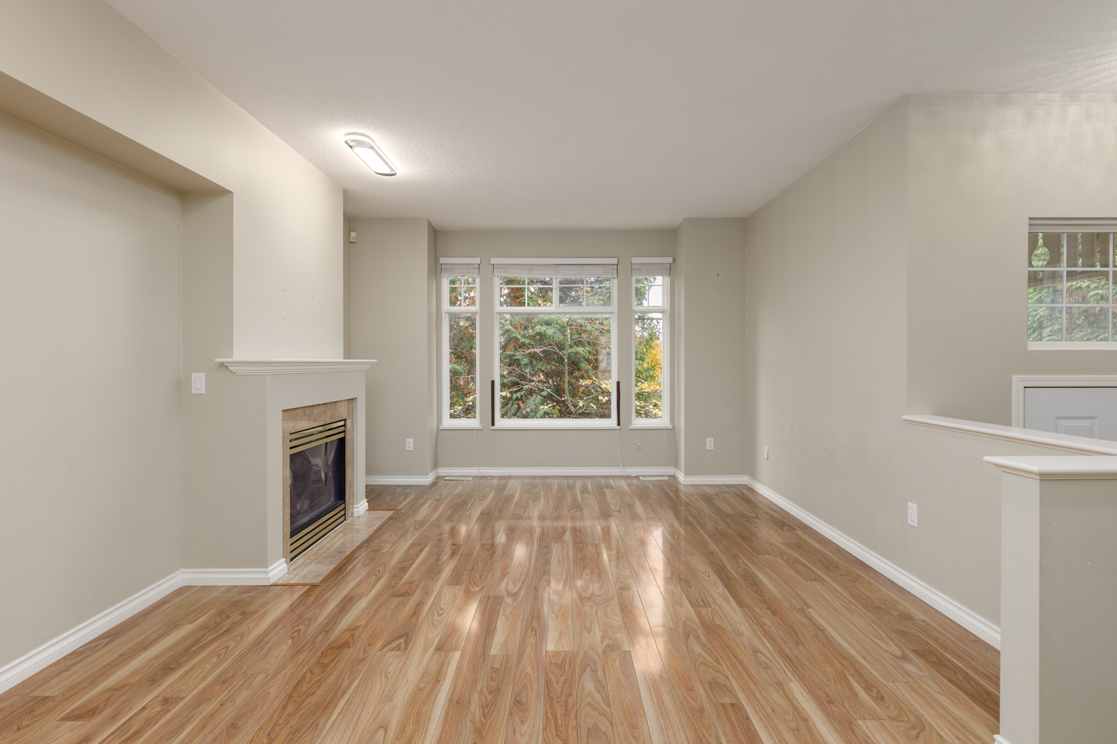 Unfurnished living room with wood flooring, a fireplace on the left, large windows at the far wall, and neutral-colored walls.