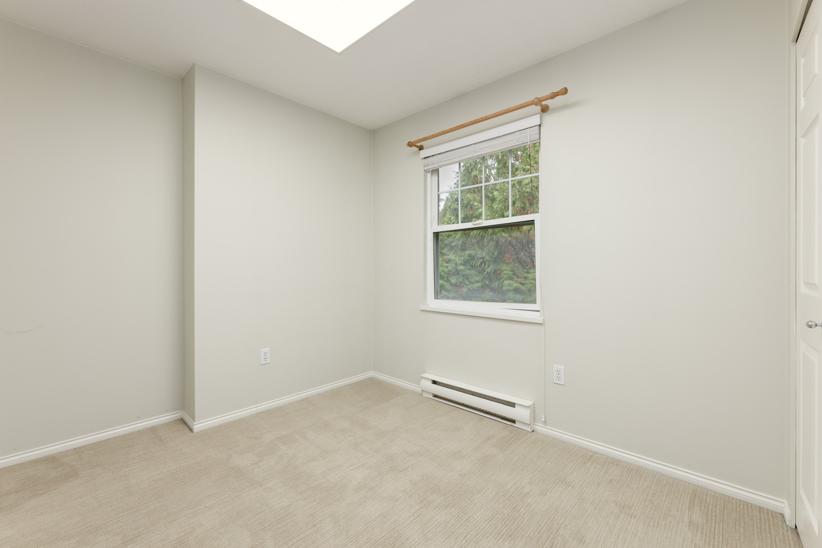 Empty room with beige carpet, off-white walls, a large window with a white frame, and a wall heater beneath the window.