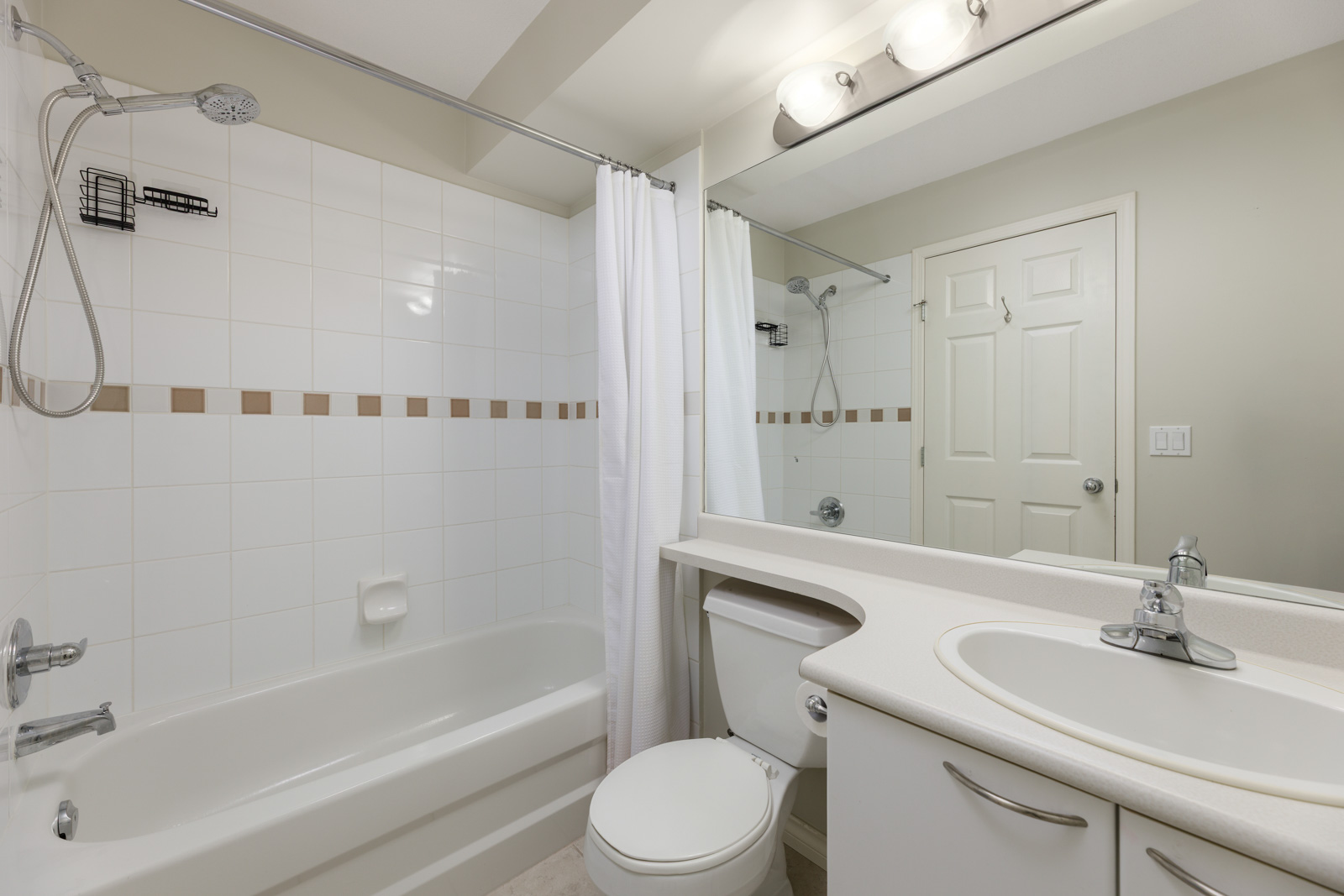 A modern bathroom with a bathtub and shower, white curtain, toilet, sink with countertop, large mirror, and overhead lighting.