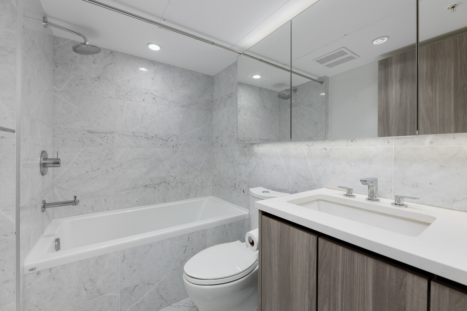 Modern bathroom with marble walls, bathtub and shower combination, toilet, and vanity with a sink and large mirror.