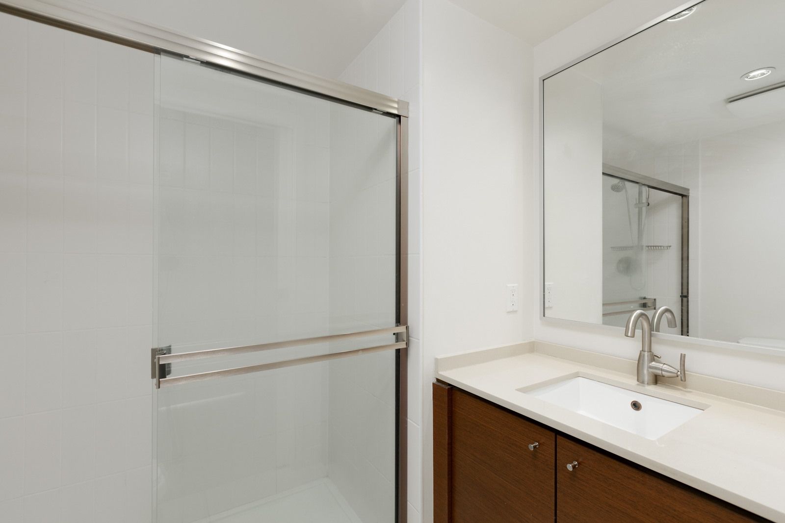 Modern bathroom with a glass-enclosed shower, a large mirror, a sink with a silver faucet, and a wooden vanity with white countertop.