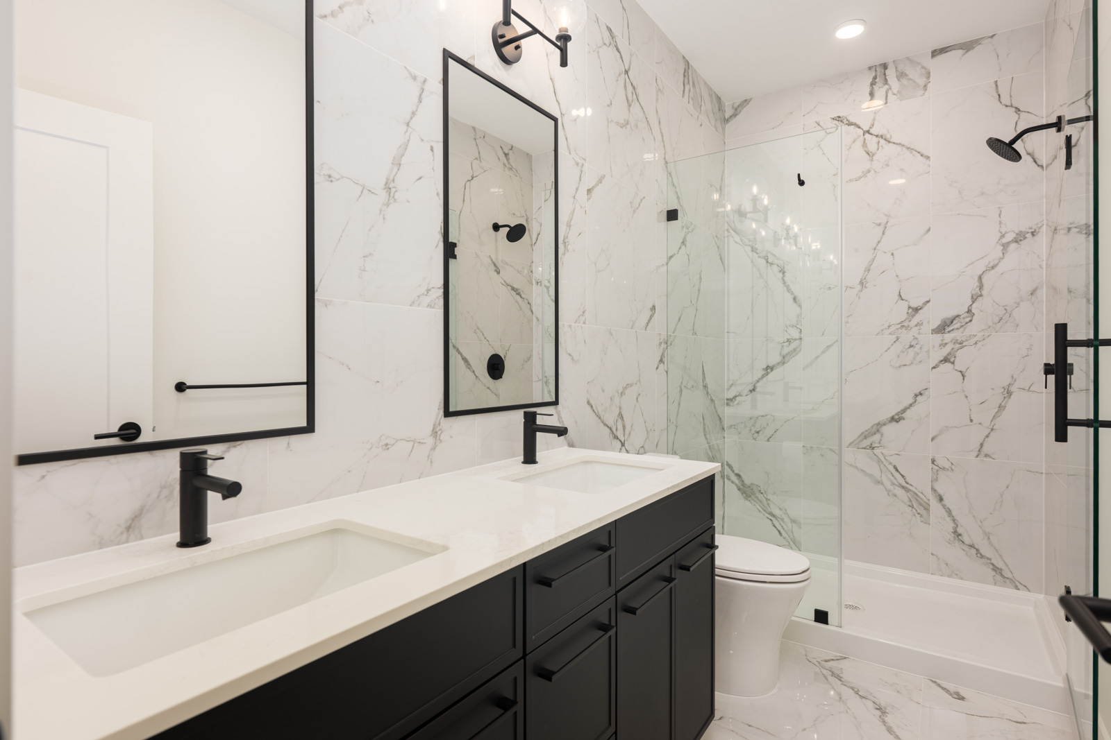 Modern bathroom with white marble walls, double sink vanity with black fixtures, large mirror, and a glass-enclosed shower.