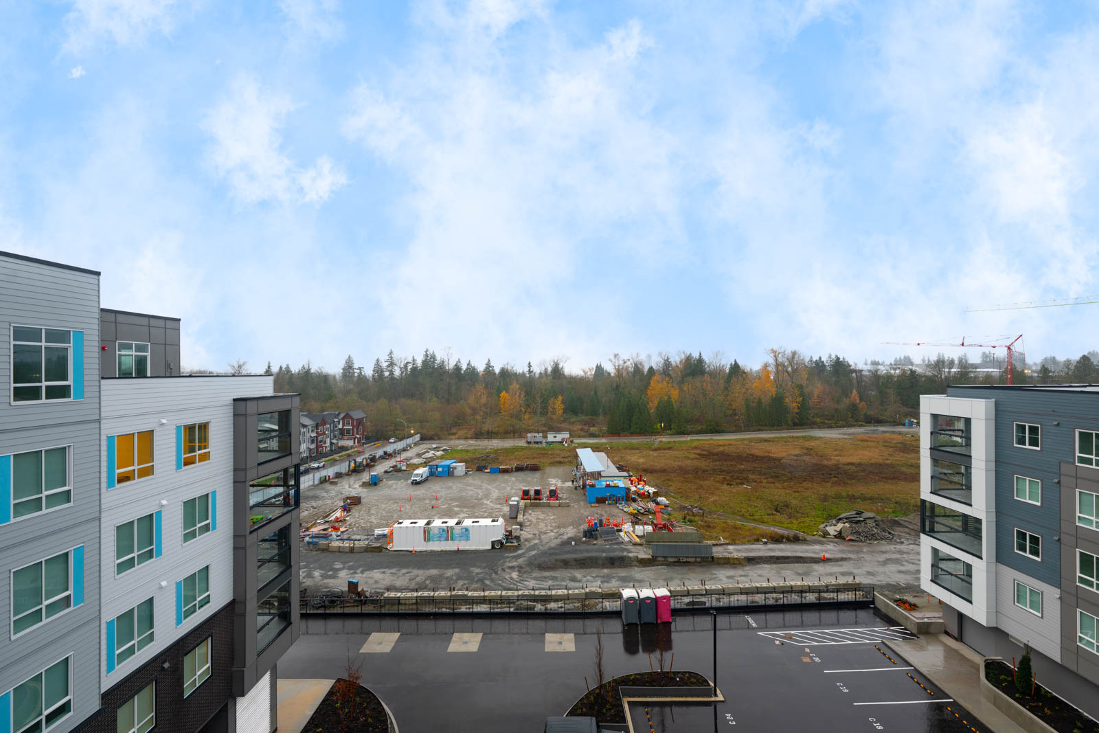 View of a construction site with scattered materials and equipment between two modern apartment buildings under a partly cloudy sky.