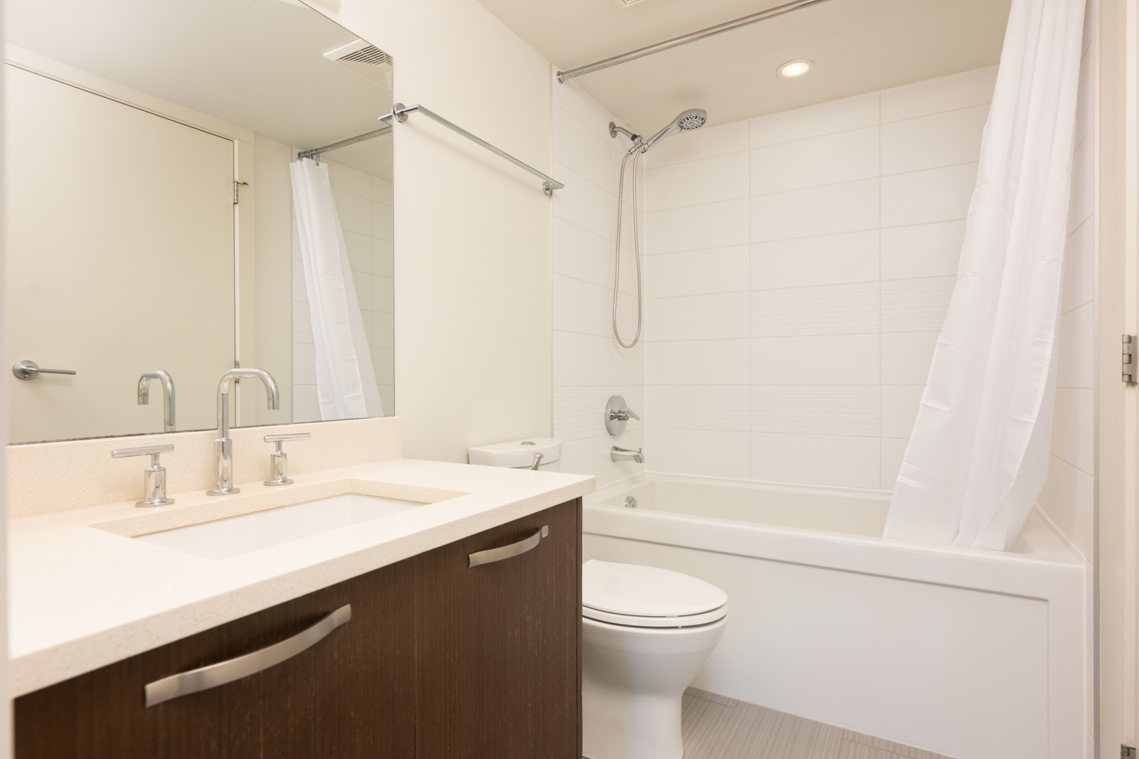 Modern bathroom with a white bathtub and shower, white shower curtain, toilet, and sink with a dark wood vanity and chrome fixtures.