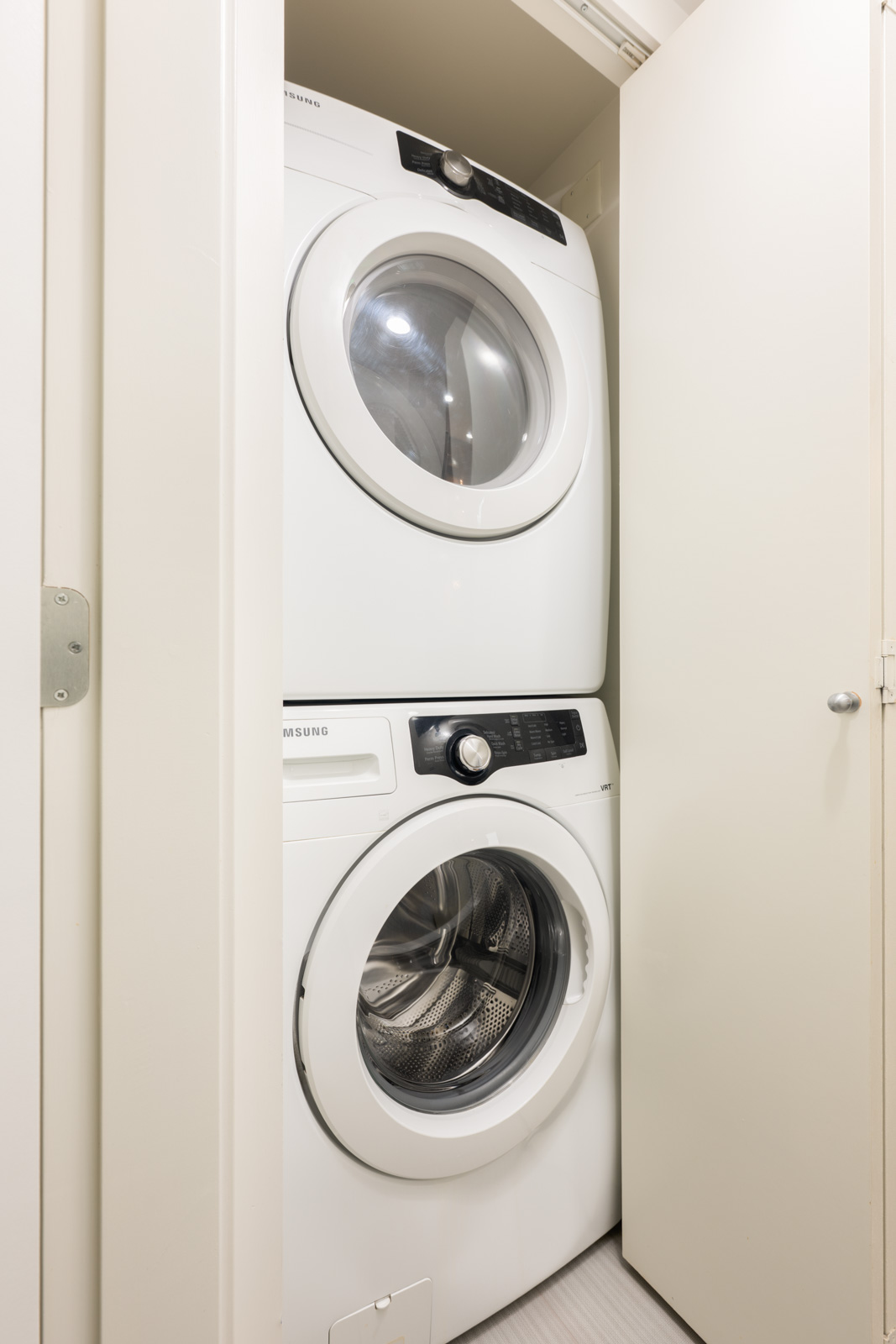 Front-loading washer and dryer stacked inside a small closet with the doors partially open.