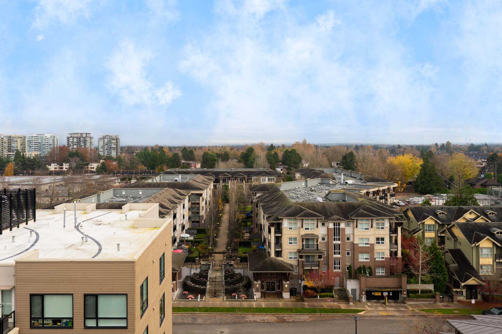 A bird’s-eye view of a residential neighborhood with multi-story buildings, trees with fall foliage, and a cloudy sky in the background.