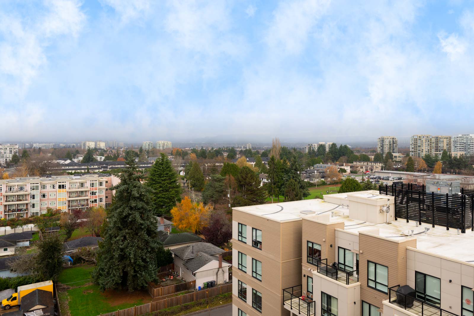 A cityscape view shows residential buildings, trees, and a partly cloudy sky with distant mid-rise apartments in the background.