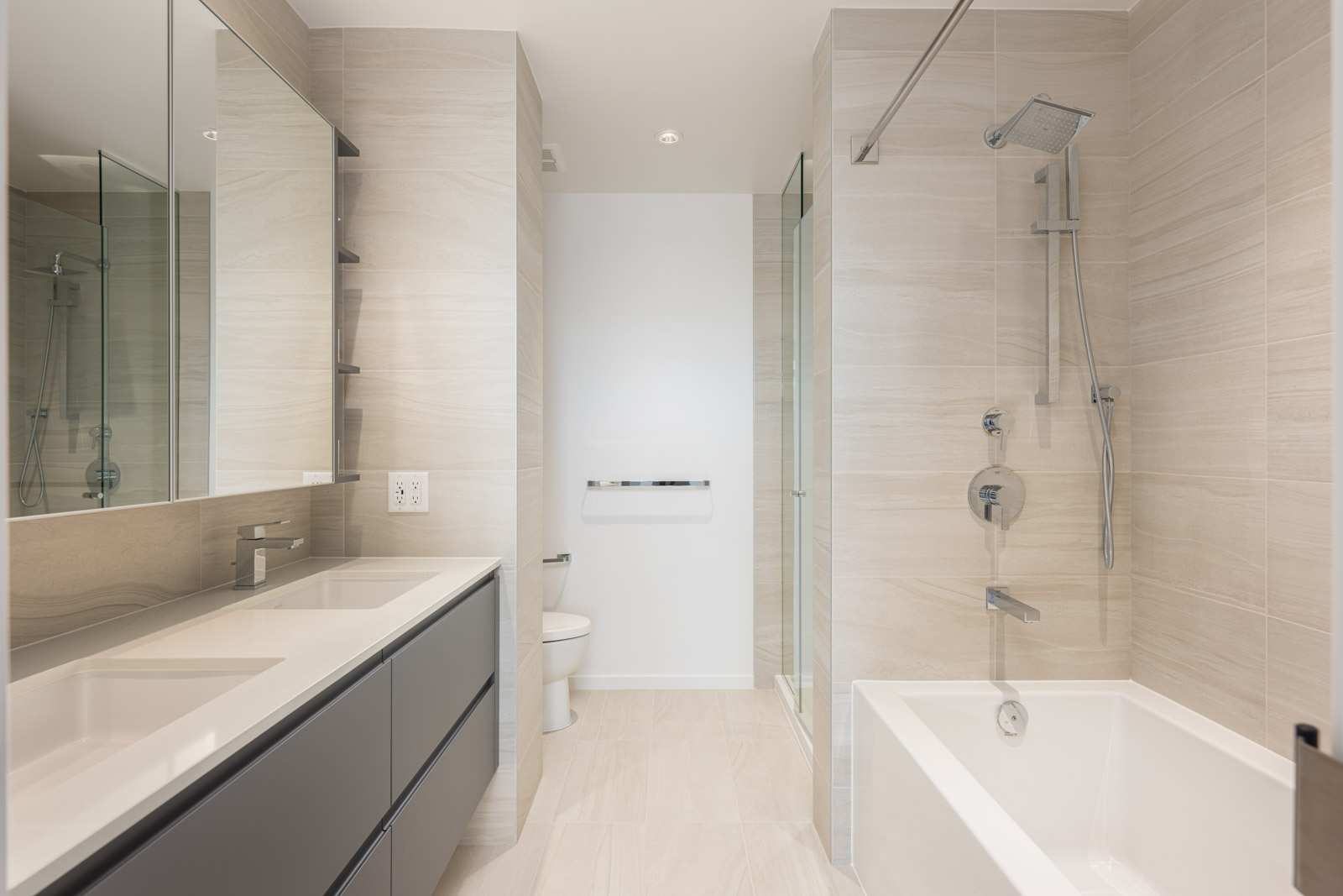 Modern bathroom with double sink vanity, wall-mounted toilet, glass shower, and bathtub, featuring neutral beige tiles and minimalistic fixtures.