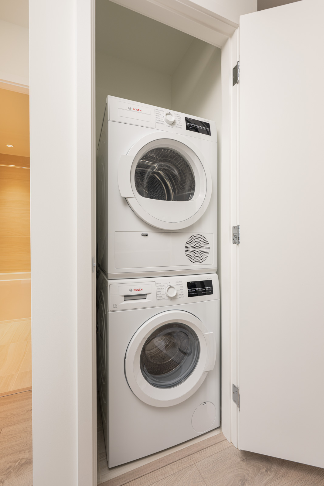 A stacked Bosch washer and dryer set in a small laundry closet with one door partially open.
