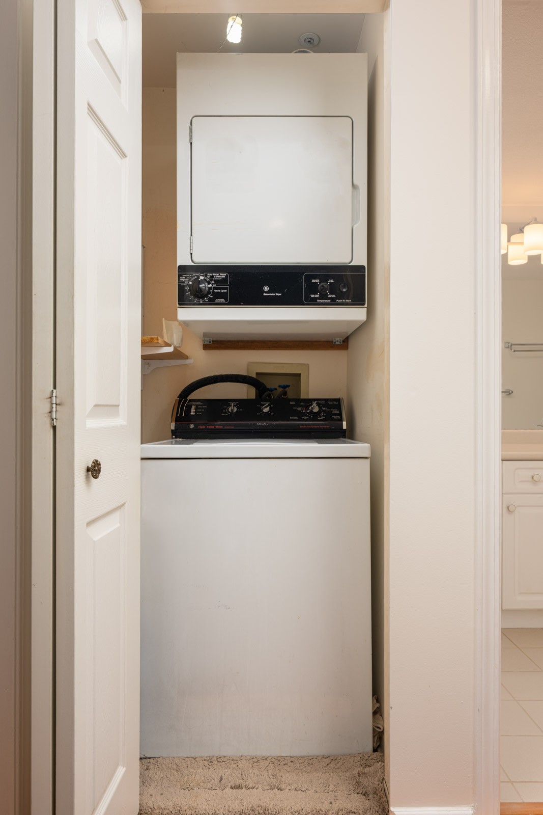 A stacked washer and dryer set is installed in a small laundry closet with an open door, adjacent to a bathroom.
