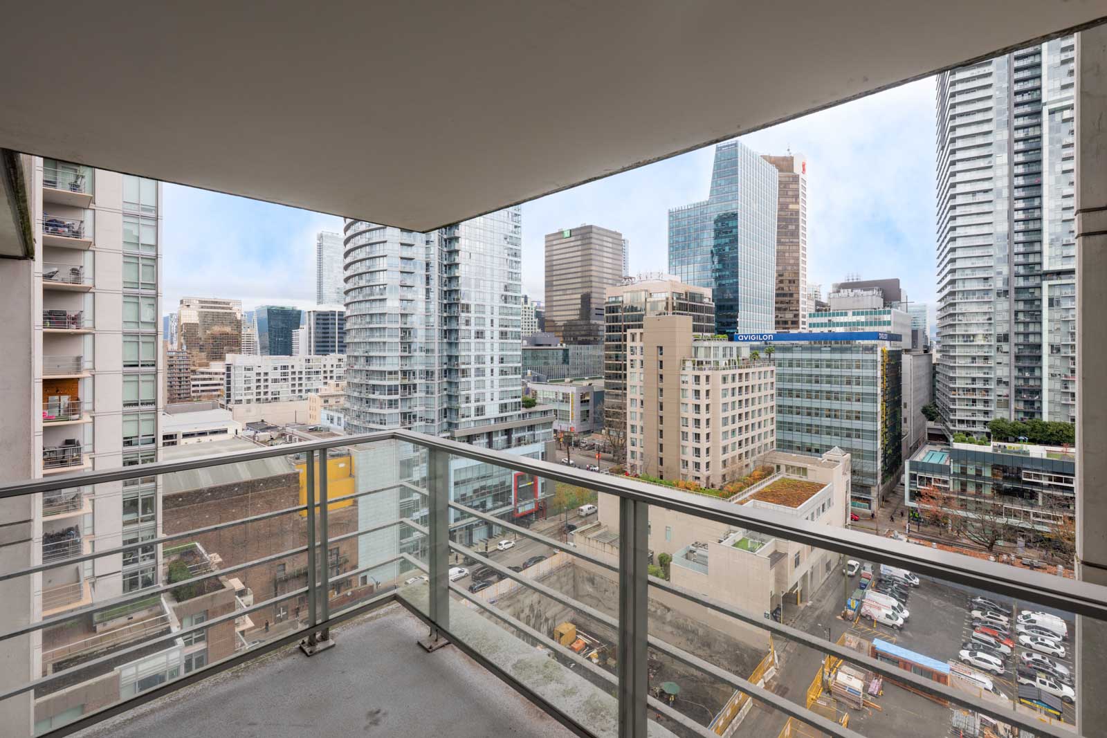View from a modern apartment balcony overlooking a cityscape with high-rise buildings, glass railings, and construction equipment below.