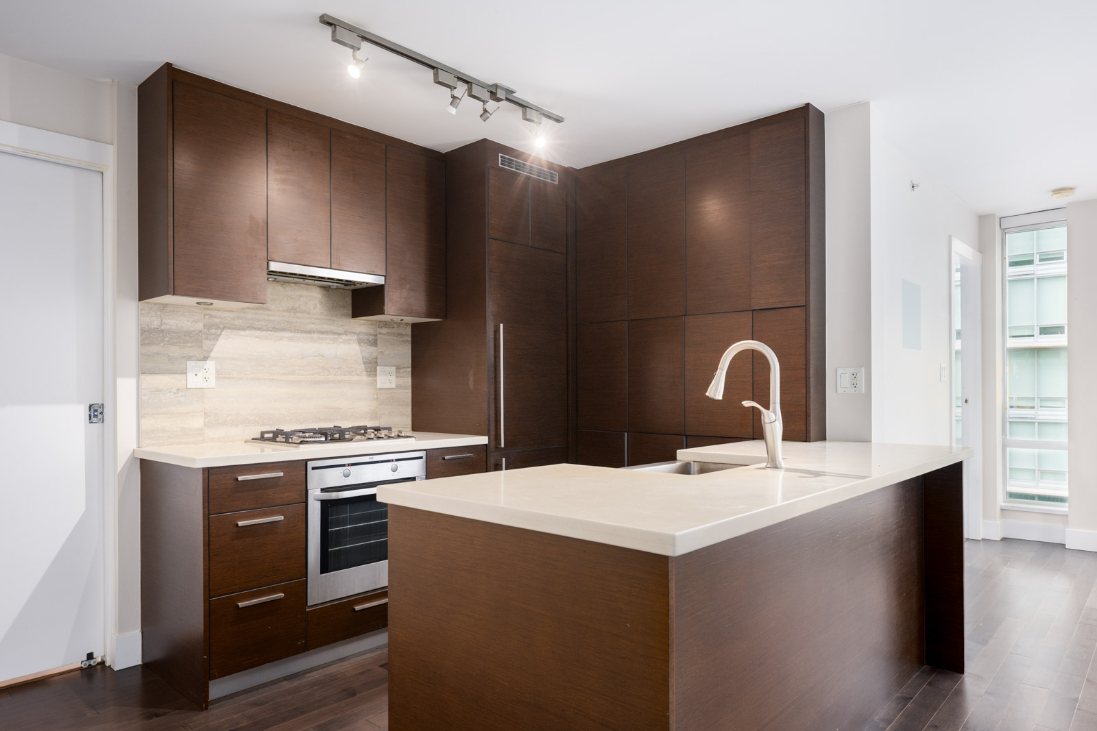 Modern kitchen with dark wood cabinets, built-in oven, gas stove, light countertops, undermount sink, and track lighting.