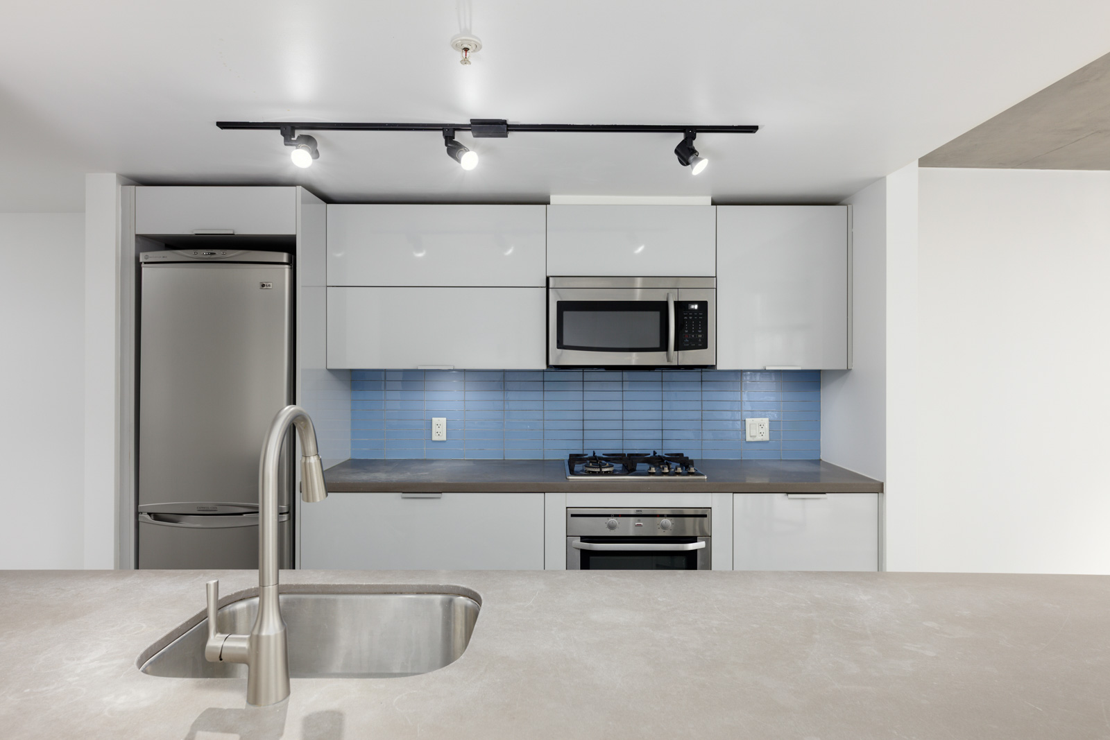 Modern kitchen with stainless steel appliances, blue tile backsplash, white cabinets, built-in oven, cooktop, and a sink in the foreground countertop.