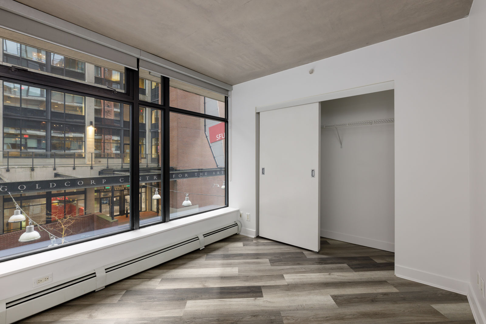 Unfurnished room with large windows, wood-look flooring, a white sliding closet door, and a view of an urban building exterior.
