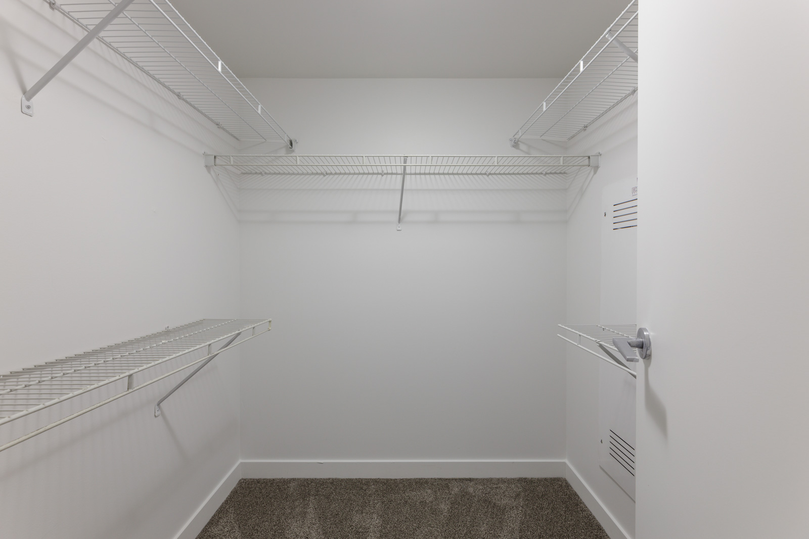Empty walk-in closet with white wire shelving on three walls, white walls, and a carpeted floor.