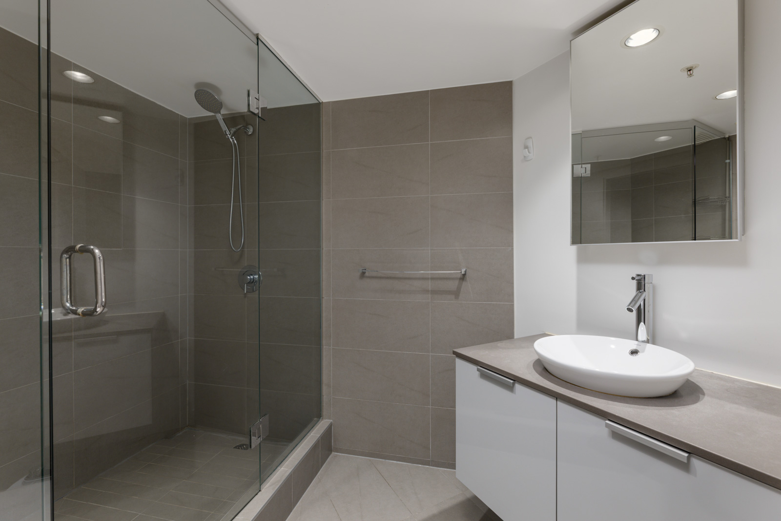 Modern bathroom with a glass-enclosed shower, gray tile walls, a floating vanity with a vessel sink, and a large mirror.