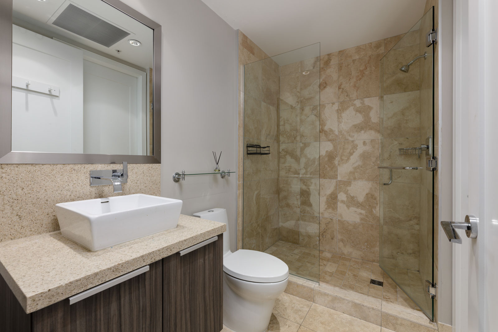 Modern bathroom with a square sink, granite countertop, toilet, and a glass-enclosed shower with beige tiles.
