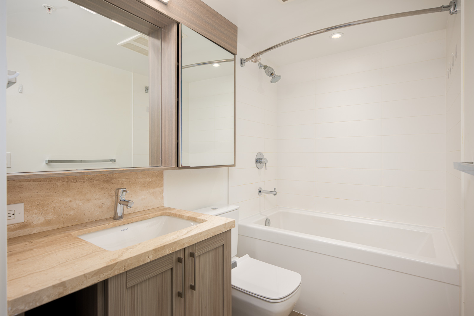 Modern bathroom with a beige countertop, built-in sink, wall-mounted mirror cabinet, white bathtub with shower, and neutral-colored tiles.