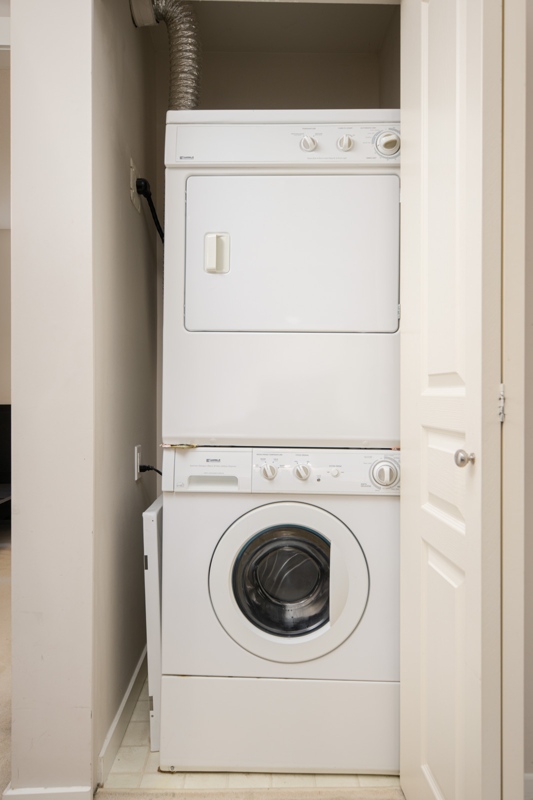 A stacked washer and dryer unit is installed in a small laundry closet with a partially open white door.