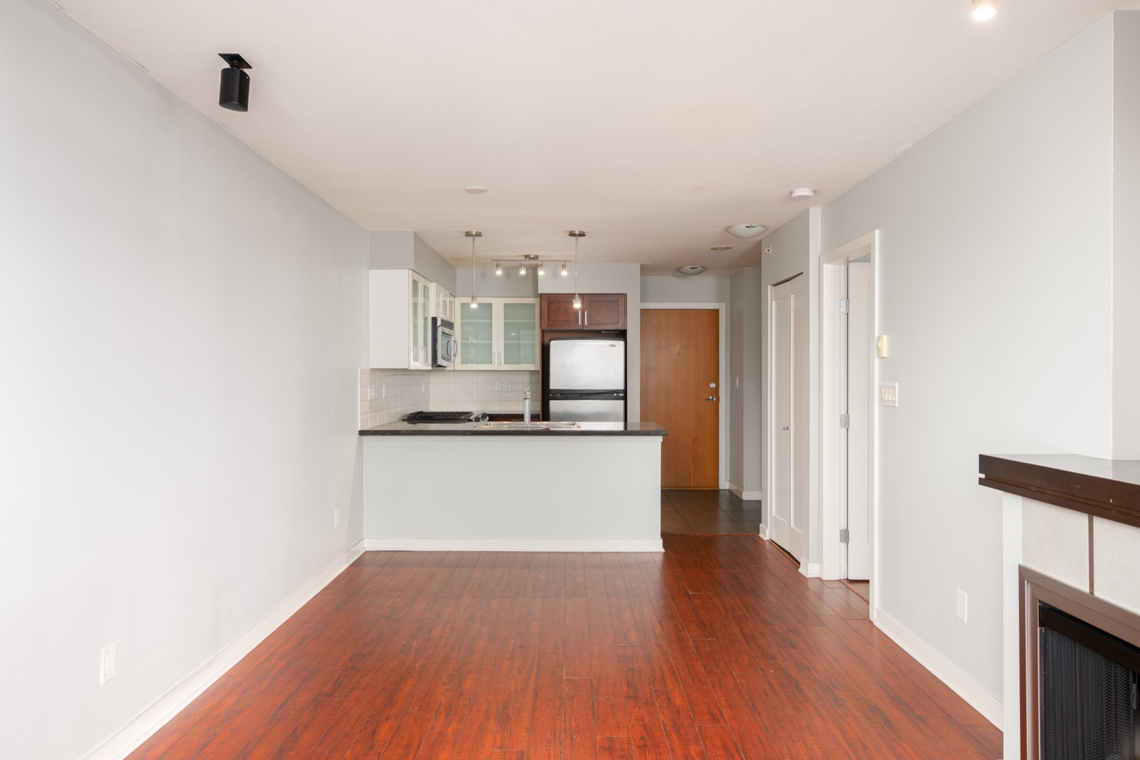 Modern apartment interior with wooden floors, an open kitchen featuring stainless steel appliances, white cabinets, and a visible entry door in the background.
